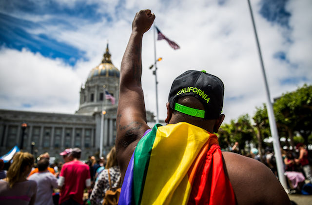 Black man with a rainbow flag raises his fist