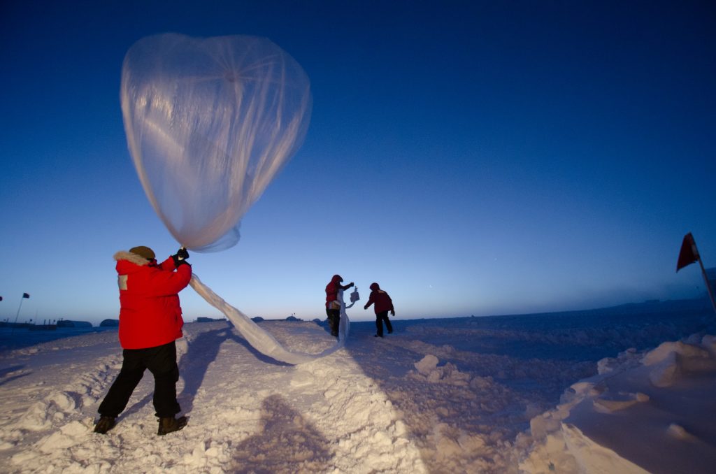 A person holding a weather balloon on top of a mountain, about to let go.