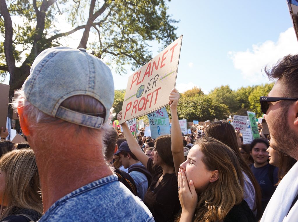 A person holding a sign that says "planet over profit" in what seems to be a large gathering of protestors