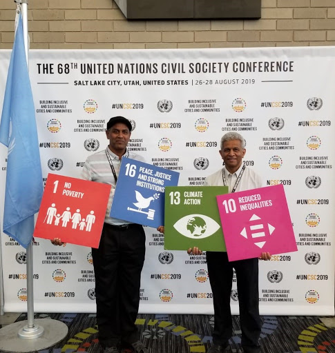 Image of two male attendees holding posters of the SDGs Numbers 1, 16, 13 and 10.