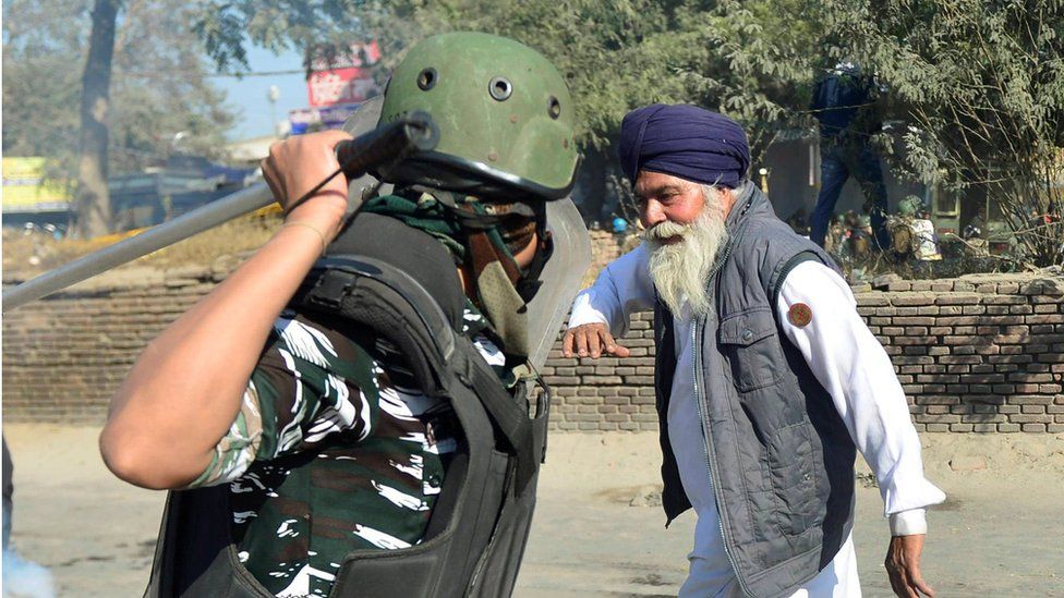 Image of an elderly Sikh man (probably a farmer) and police officer with his baton raised about to hit the man