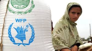 Image of a young girl sits next to a bag stamped with the WFP logo