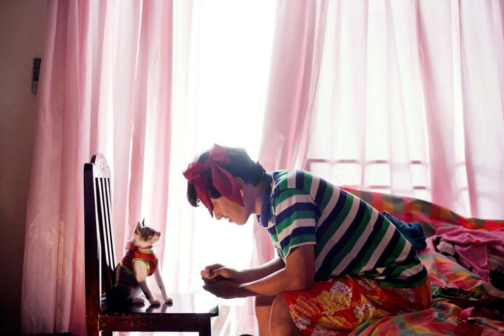 A kitten on a chair and a woman. Both looking into each other's eyes. 