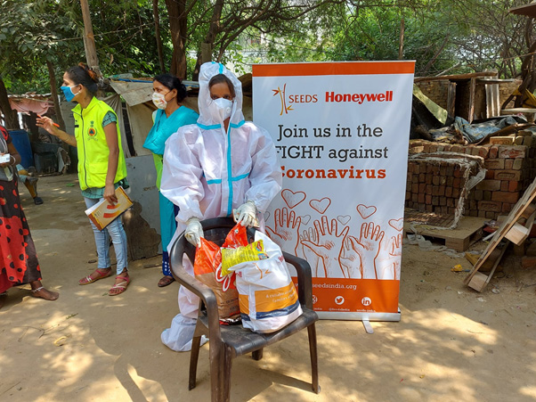 Women wearing masks and PPE kits near a SEEDS India banner. 