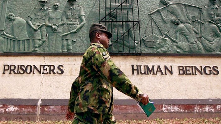 An image of a Sri Lankan soldier walking past the front wall of the Welikada prison which reads 'Prisoners are human beings'