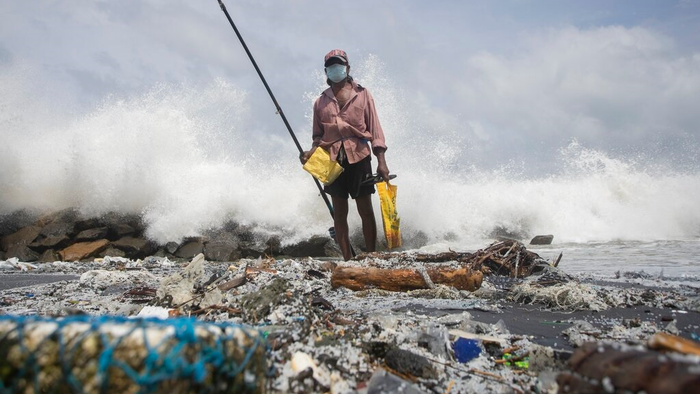 An image of plastic nurdles coating the coastline of Sri Lanka, with a fisherman in the background