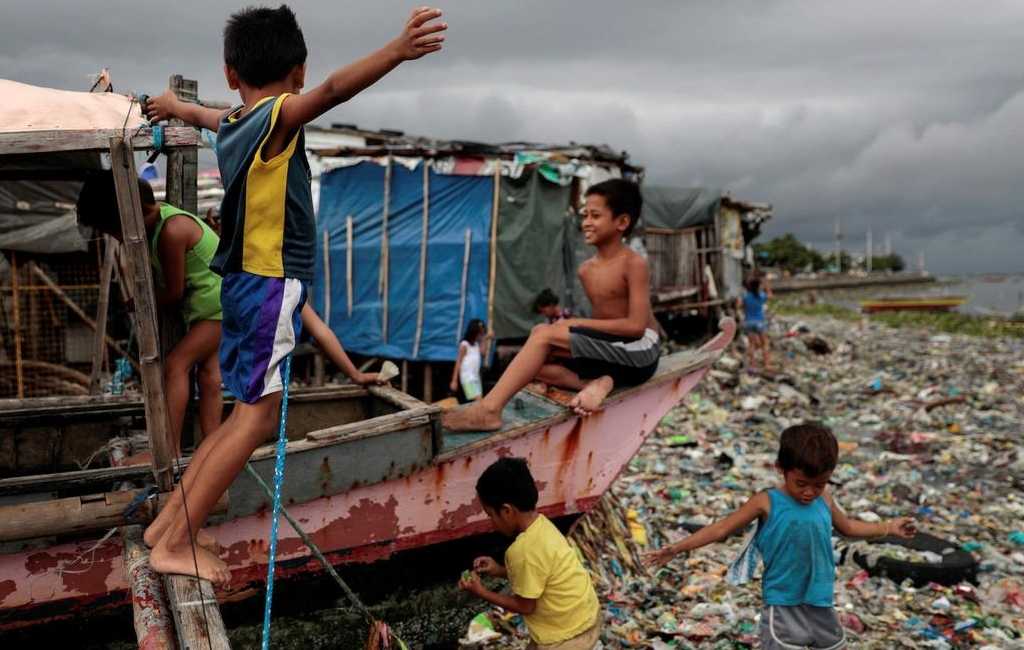 Children playing on a boat docked near a pile of garbage. 