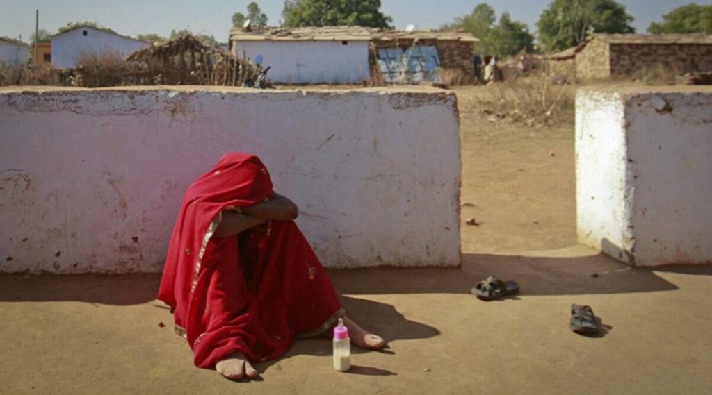 Image of a barefooted girl sadly sitting on floor with a child feeder and poor surrounding.