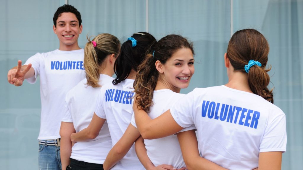 a group of people are smiling and wearing t-shirts that indicate that they are volunteers