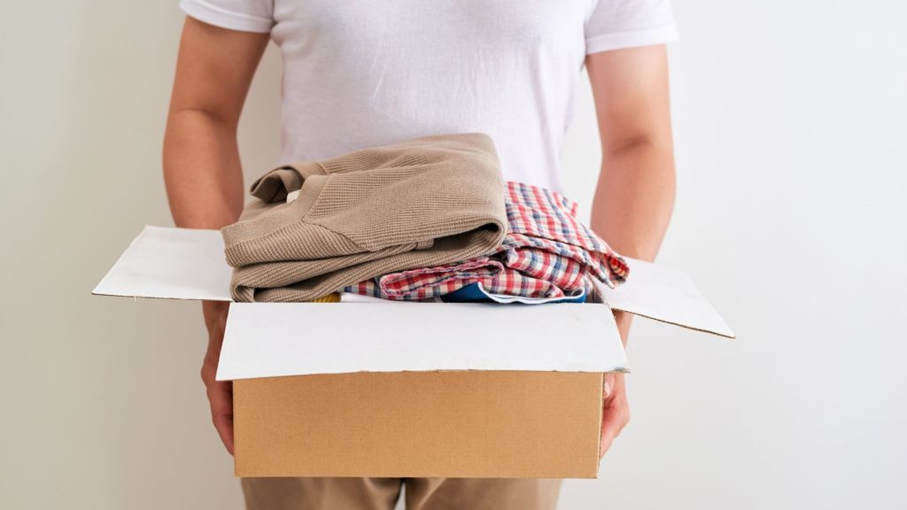 person holding a cardboard box of clothes in their hands.