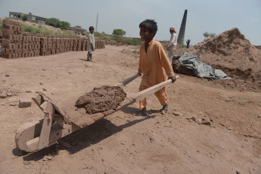 A child labor in Pakistan pushes a hand-made cart at a brick kiln, one of the dens of bonded labour