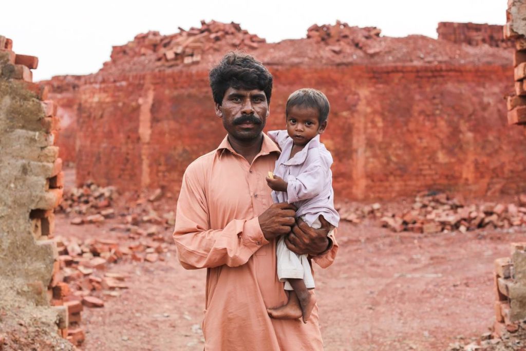 A bonded labourer stares at the camera while holding his young son at a brick kiln in Pakistan