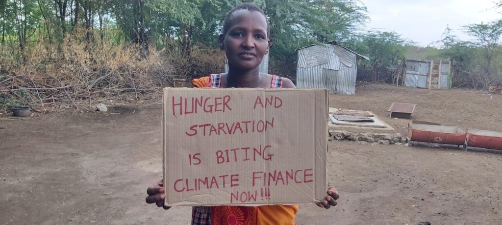 An image of an African child holding a banner written " Hunger and starvation is bitting, Climate finance now.