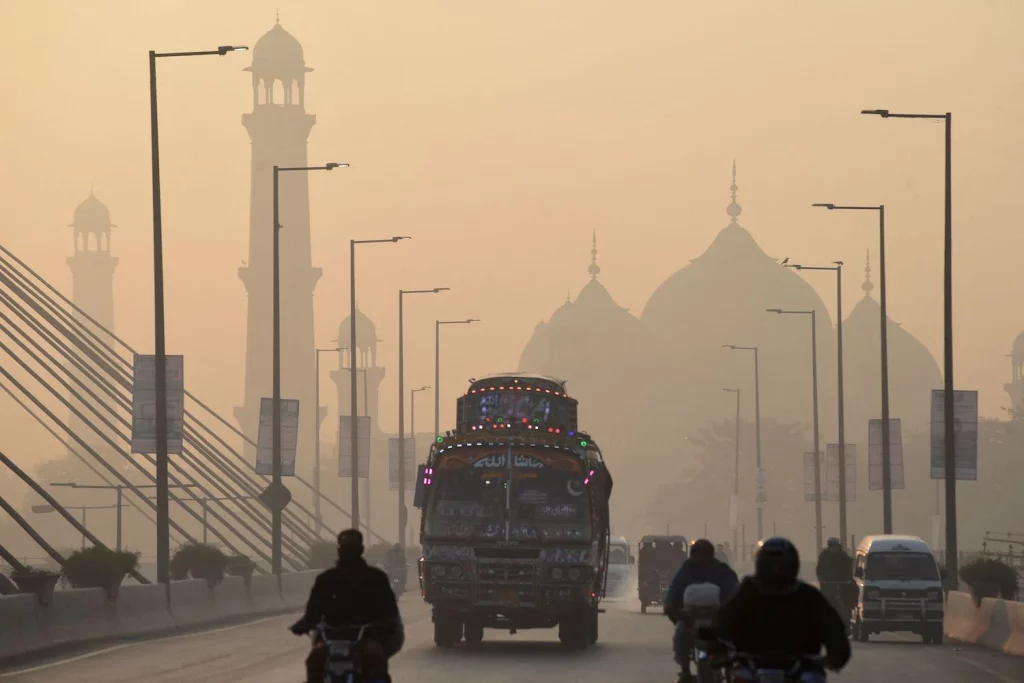 A blanket of smog envelops a busy road in Lahore and reduces visibility thereby blurring buildings in the background.